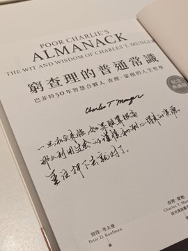 A close-up of the book "Poor Charlie's Almanack: The Wit and Wisdom of Charles T. Munger" with Chinese characters on the cover, featuring a handwritten note in Chinese from "Peter D. Kaufman".