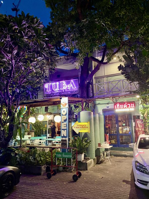 An evening view of a restaurant named 'TUBA Italian Restaurant & Restaurant' with a purple neon sign, an 'OPEN' banner, and a 'TUBA THANKS' cart in front.