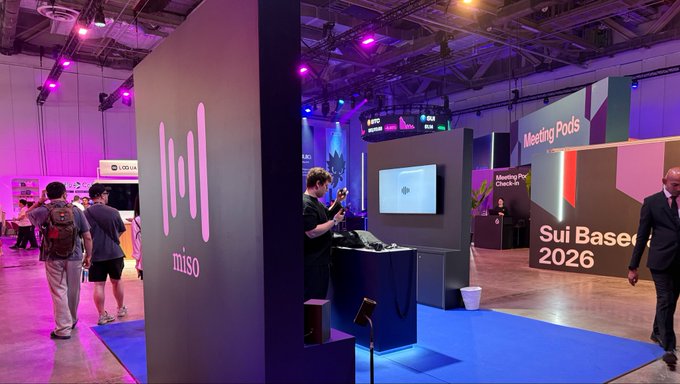 A photo of a convention or trade show floor featuring a 'miso' booth with audio waves logo, alongside displays reading 'Sui Based 2026' and 'Meeting Pods.'