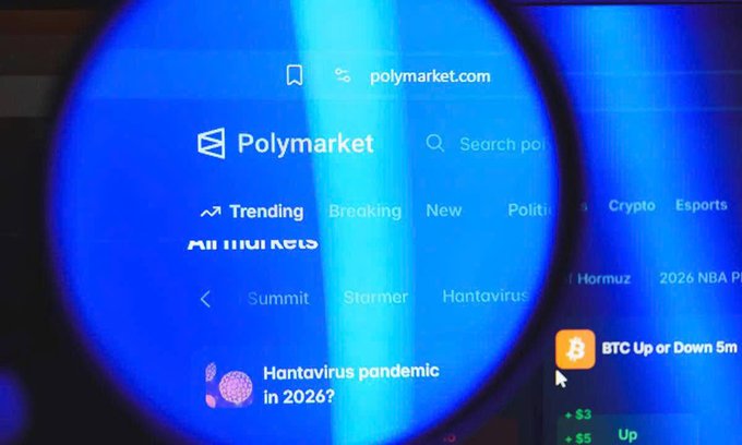 A magnifying glass zooms in on Polymarket's homepage, displaying navigation tabs like "Trending," "Breaking," "Crypto," and market titles including "Hantavirus pandemic in 2026?" and "BTC Up or Down 5m," visually connecting to the platform's new launch of perpetual crypto futures trading with up to 20x leverage on assets like Bitcoin.