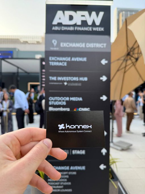 The image features a person holding up a business card for "Honey Bee Automotive", which seems to be related to the ADFW Abu Dhabi Finance Week event. The card has a logo of an umbrella with the text "Honey Bee Automotive" written on it, and there is also a picture of an umbrella in the background. This suggests that the person holding up the business card might be promoting their services or products at the event.