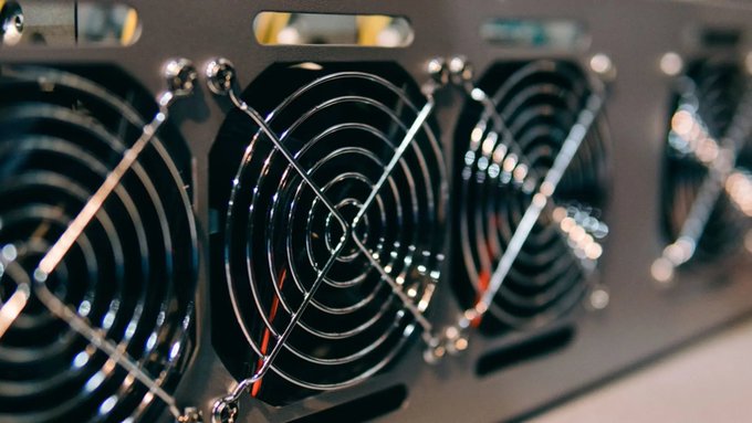 Close-up photograph of multiple black computer cooling fans with protective wire grilles mounted in a metal frame, likely from a mining rig or server.