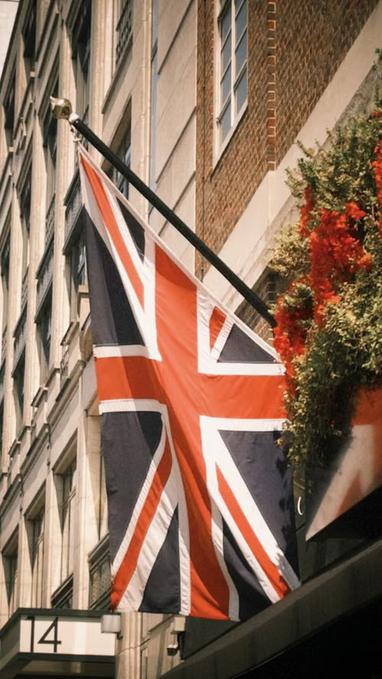 A Union Jack flag hangs from a building displaying the number "14," likely a Bank of England-adjacent structure in London. The flag symbolizes Britain's national identity as the country positions itself to lead in stablecoin and crypto innovation.