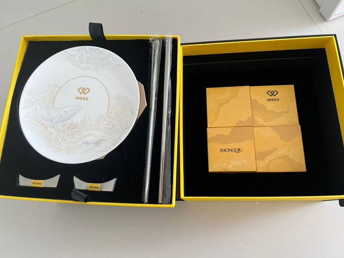 An open black and yellow gift box containing a white porcelain plate with whale and wave designs branded 'WEEK', chopsticks, rests, and four orange mooncake boxes labeled 'WEEK' and 'ZHONGQIU'.