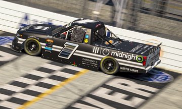 The image features a black truck racing down a track, with the word "Cardano" visible on its side. The truck appears to be participating in an event or race, as indicated by the text in the caption. The truck's design is unique, featuring a logo and the words "Cardano" and "Midnight". This truck seems to be racing against other vehicles during a competition.