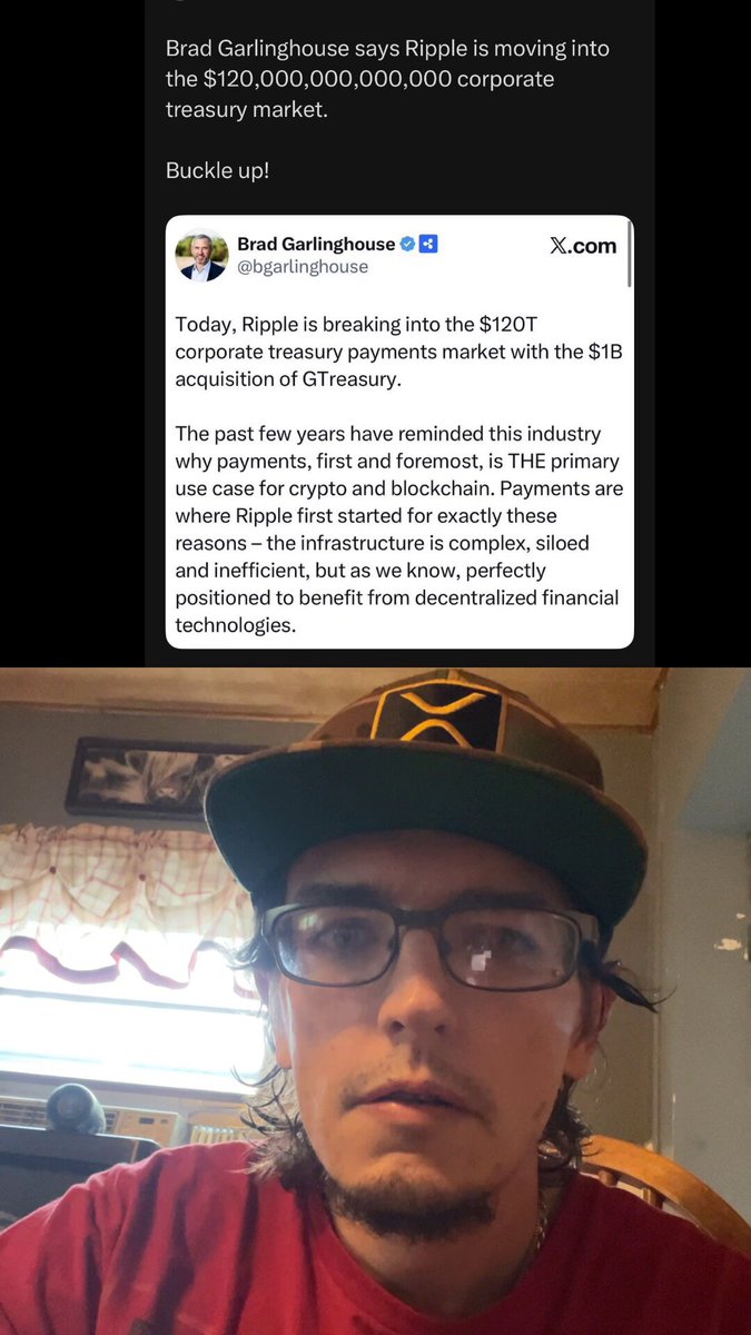 The image features a man wearing glasses, a red shirt, and a green baseball cap with an X on it. He appears to be sitting at a desk or table while looking directly into the camera. The background of the photo shows a computer screen displaying a message about the Treasury Market.