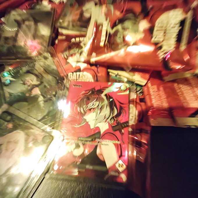 A blurry, close-up photo of what appears to be holographic anime collectible cards or stickers, with a prominent red card featuring a female character visible in the center.