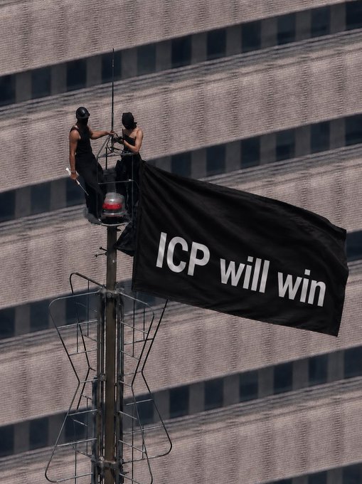 Two masked individuals perched atop a tall pole are unfurling a large black banner reading "ICP will win," which directly promotes the $ICP cryptocurrency token displayed in the post.