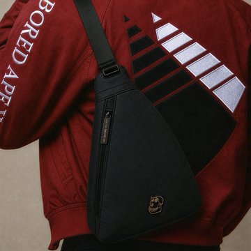 A person wearing a red 'BORED APE' jacket with a black triangular chest bag featuring a zipper and a small skull logo patch.