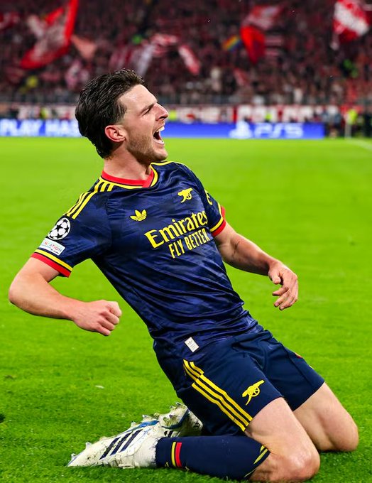 A Real Madrid player in a dark blue “Emirates Fly Better” kit kneels on the soccer field and celebrates.