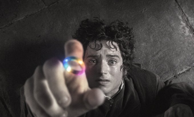 A still from a film showing a young man with curly dark hair reaching out with his hand toward the camera, a glowing rainbow ring visible on his finger, appearing distressed.