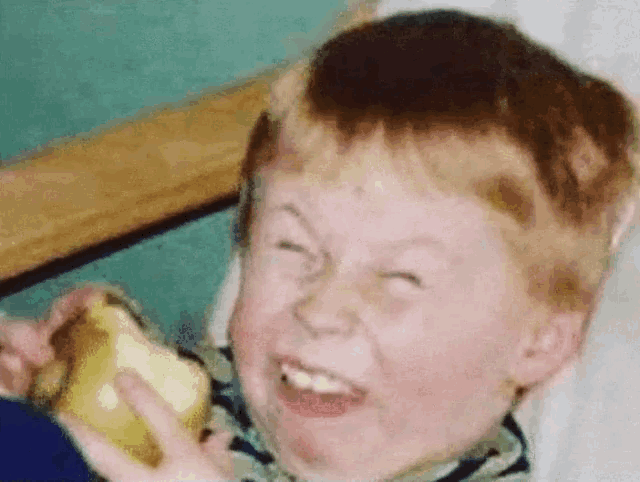 A vintage-style photograph of a red-haired boy smiling and biting into a piece of food, possibly an apple or pastry, against a teal background.