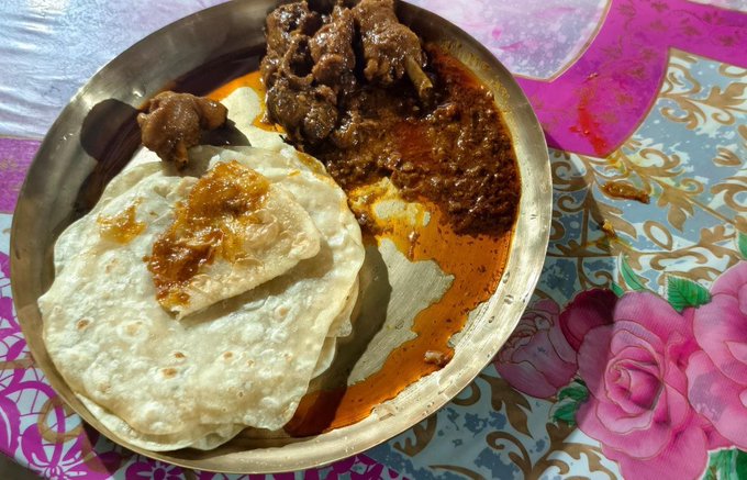 A plate of Indian food featuring flatbread (roti or paratha), a meat curry, and a red lentil or bean dish, served on a floral-patterned tablecloth.