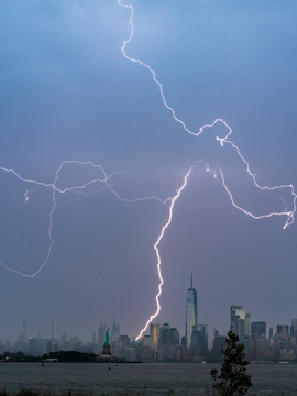 A dramatic lightning storm illuminates the New York City skyline, including One World Trade Center, across the water.