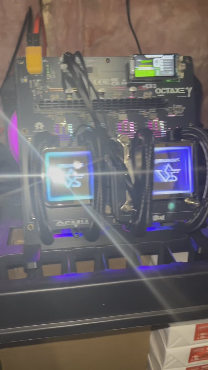 A close-up photograph of a computer motherboard with RGB-lit "OCTAXEY" branded cooling blocks and components illuminated in blue and purple lighting.