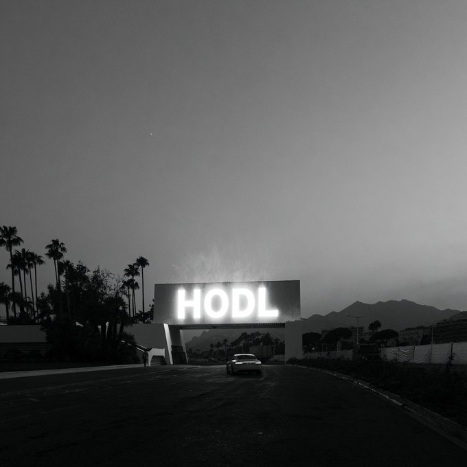 A glowing "HODL" sign illuminates a dark desert highway as a lone car drives toward it, evoking the welcoming sentiment "We'll leave the light on for you" from the crypto community to a departing trader. The illuminated billboard stands as a beacon of steadfast holding amid an empty road and twilight sky.
