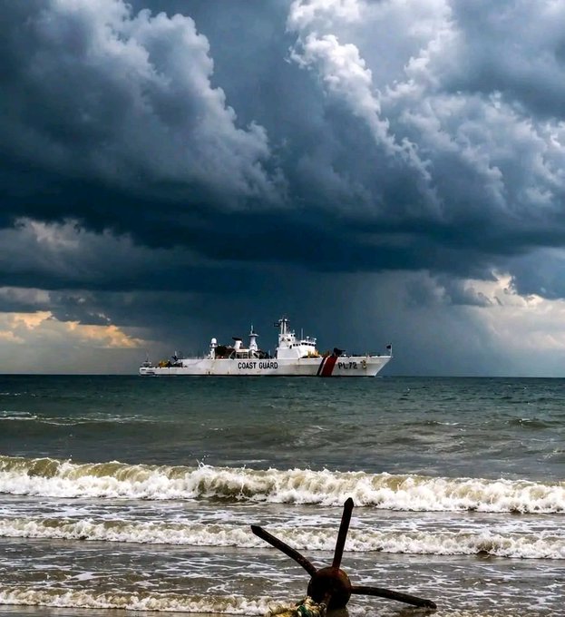 A Coast Guard ship marked "COAST GUARD" sails under ominous storm clouds off the shoreline, with a rusted anchor visible in the foreground surf—symbolizing the turbulent market conditions as BTC holds above $69K and ETH around $2.2K.