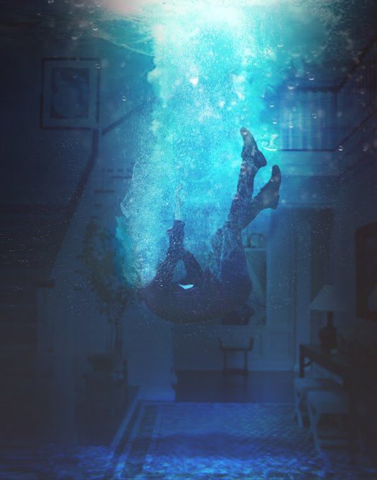 A surreal image of a person appearing to float upside down underwater inside a house, illuminated by blue light with bubbles rising around them.
