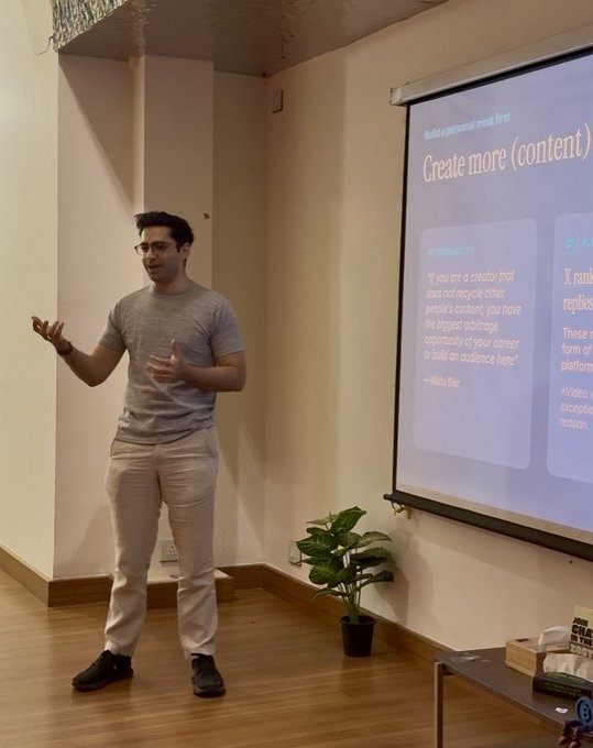 A man gives a presentation in front of a projection screen displaying the slide "Create more (content)" with a quote attributed to Nikita Bier: "If you are a creator that does not recycle other people's content, you have the biggest arbitrage opportunity of your career to build an audience here!" The setting reflects the post's context of a GTM session with builders at @joinosmosis during the speaker's time in Bangalore.