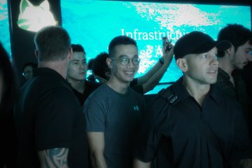 Three men at an Infrastructure event, with one wearing a gray shirt and glasses smiling, and another in a black shirt and cap looking to the side.
