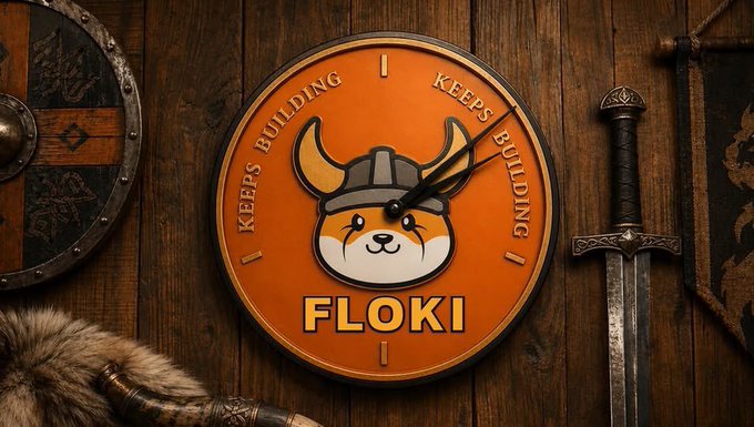 An orange wall clock featuring a Shiba Inu dog wearing a Viking helmet with the text 'KEEPS BUILDING' and 'FLOKI', surrounded by medieval items like shields and a sword.
