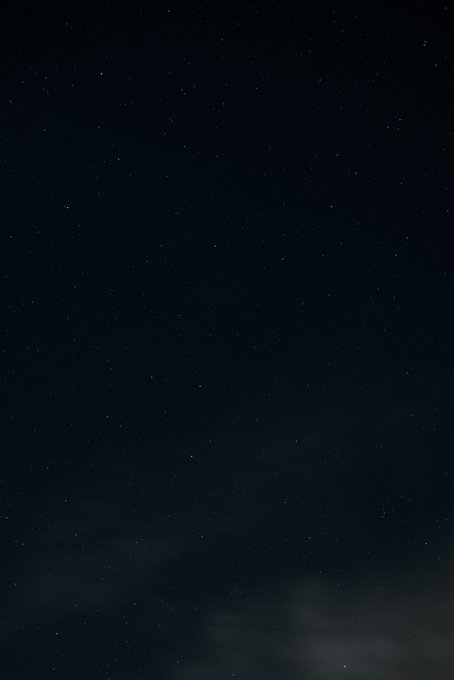 A nearly black image of a night sky with faint stars visible and subtle cloud wisps at the bottom.