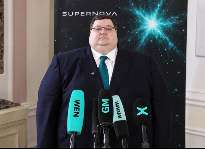 A man in a dark suit and teal tie stands at a press conference in front of a "SUPERNOVA" backdrop featuring a cosmic graphic, with multiple microphones labeled "WEN," "GM," "WAGMI," and "X" lined up before him. The "big day" caption reflects the formal announcement setting, with the crypto-inspired mic labels (WEN, GM, WAGMI) suggesting a significant Web3 or crypto-related reveal.