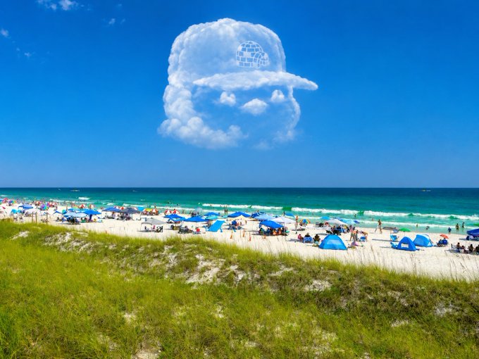 A sunny beach scene with white sand, turquoise water, blue umbrellas, and beachgoers, featuring a surreal cloud shaped like a face wearing sunglasses in the sky.