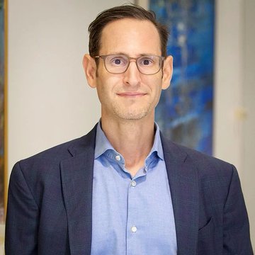 Matthew Sigel, VanEck's Head of Digital Assets Research, is pictured smiling in a blue shirt and blazer. The image accompanies commentary from him identifying Strategy's recent Bitcoin sales as a "newspaper headline bottom," coinciding with all 12 of VanEck's capitulation signals flashing simultaneously—a historically rare occurrence suggesting a potential major Bitcoin bottom.
