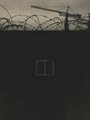 A dark, low-light image showing the silhouette of a wall topped with barbed wire and a small window or opening.