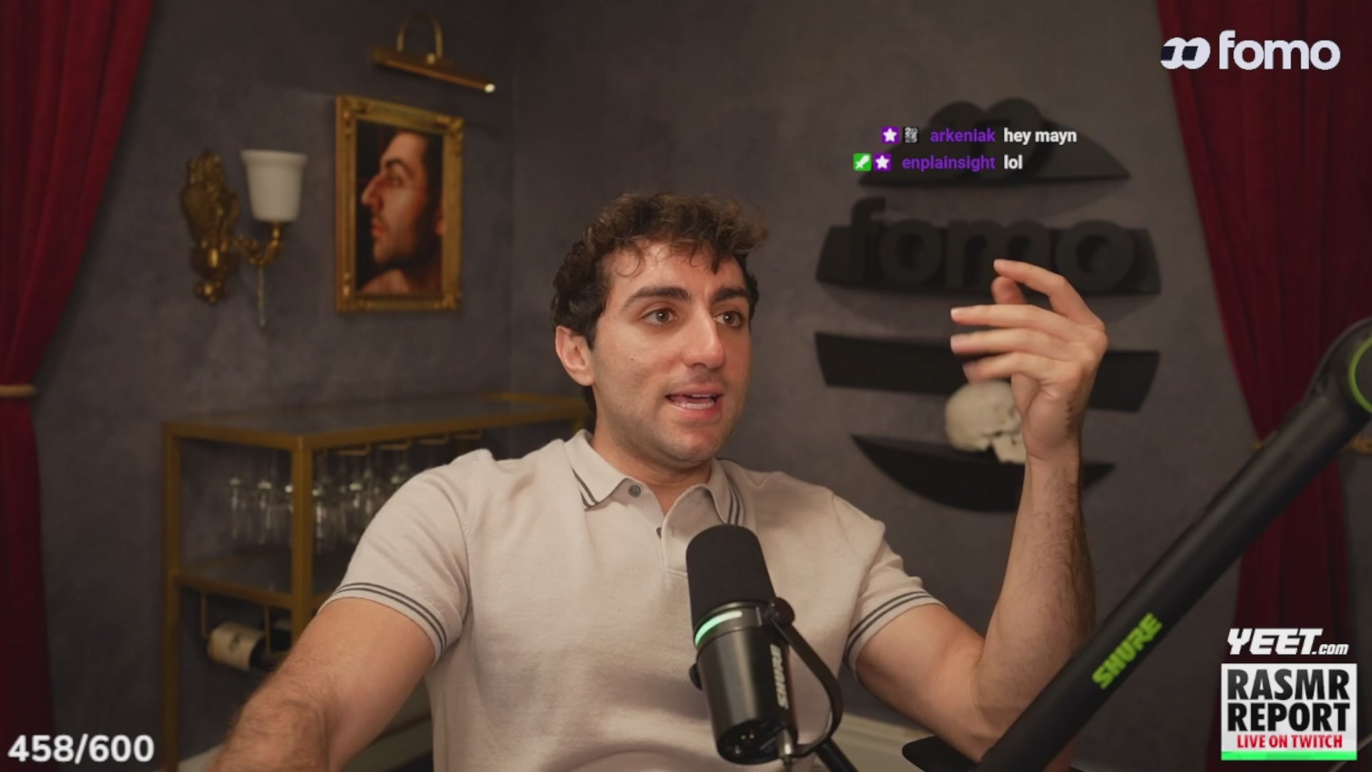 urns of water, a portrait, and a lamp are displayed on the wall behind a man speaking into a microphone at a podcast recording studio.