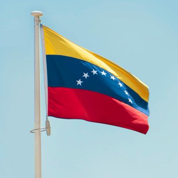 The Venezuelan flag waves against a clear blue sky, illustrating the nation's move to integrate Bitcoin into its national banking system. This image symbolizes Venezuela's embrace of cryptocurrency.