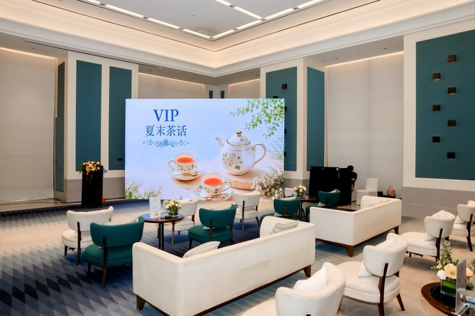 An elegant indoor lounge area is set up for an event, with a large screen displaying 'VIP 夏季茶话' (Summer Tea Party) alongside images of tea sets and pastries.