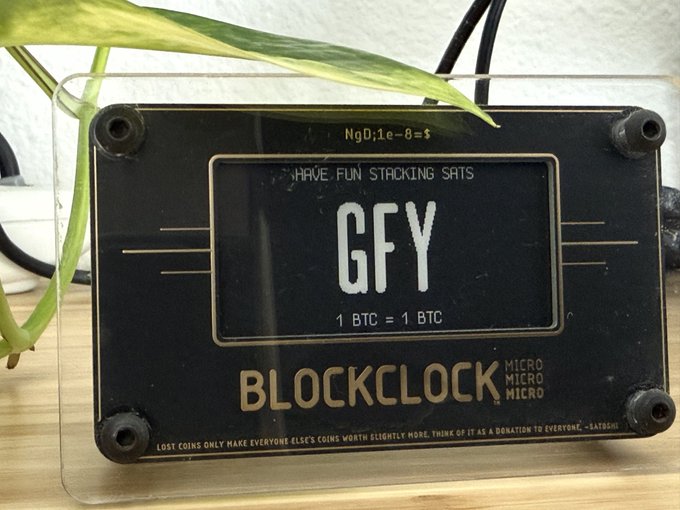 A Blockclock Micro device displays 'GFY', 'HAVE FUN STACKING SATS', and '1 BTC = 1 BTC', with text reading 'BLOCKCLOCK' and 'LOST COINS ONLY MAKE EVERYONE ELSE'S COINS WORTH SLIGHTLY MORE. THINK OF IT AS A DONATION TO EVERYONE.'