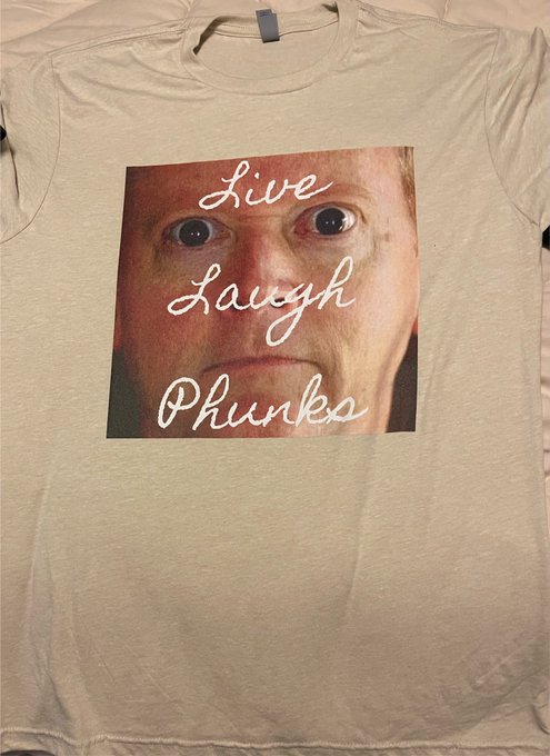 A tan t-shirt featuring a graphic print of a close-up face with the text 'Live Laugh Phunks' overlaid in white script.