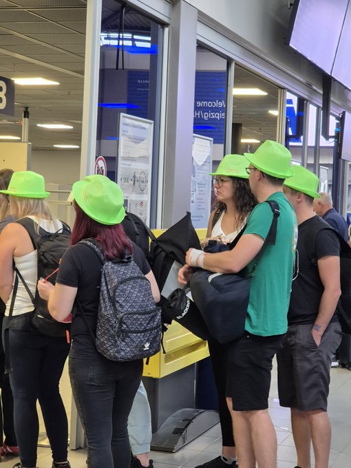 A group of travelers wearing matching bright green hats standing in line at what appears to be an airport check-in or boarding gate.