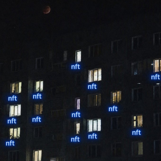 A nighttime photograph of an apartment building with several illuminated windows, edited so that the glowing blue text 'nft' appears in the unlit windows beneath the lit ones, under a dark sky with a red moon.