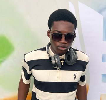 A young boy wearing sunglasses, silver headphones around his neck, and a black and white striped polo shirt poses for the camera.