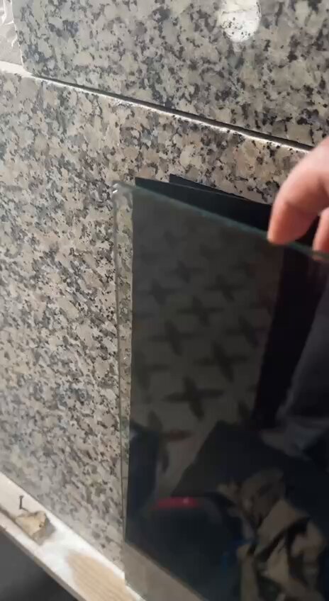 The image shows a person holding up a black glass window, possibly a window screen or a piece of artwork, against a wall with gray tiles. The text "GTD and FCFS Who needs a spot?" suggests that someone might be looking for a specific area on the wall where they can place their glass item.