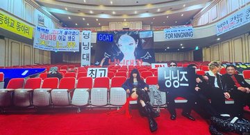 A group of people pose in an auditorium with red seats, holding various signs including "GOAT," "FOR KINGNONG," and Korean text, with "LAMBO" visible on the screen behind them. The humorous post suggests Stellar Lumens (XLM) is only for beginner cryptocurrency investors, contrasting with the Lamborghini-themed imagery that implies wealth and success.
