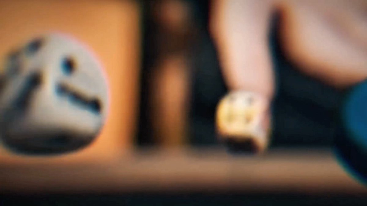 A heavily blurred, close-up image showing what appears to be a white object with black markings and a hand with a ring on a finger.