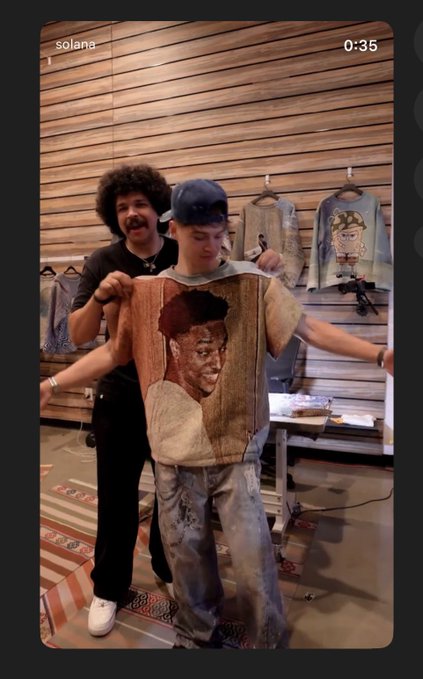 Two men in a wood-paneled clothing shop pose with a tapestry-style shirt featuring a portrait of a young man; 'solana' is visible at the top of the Snapchat story at 0:35.