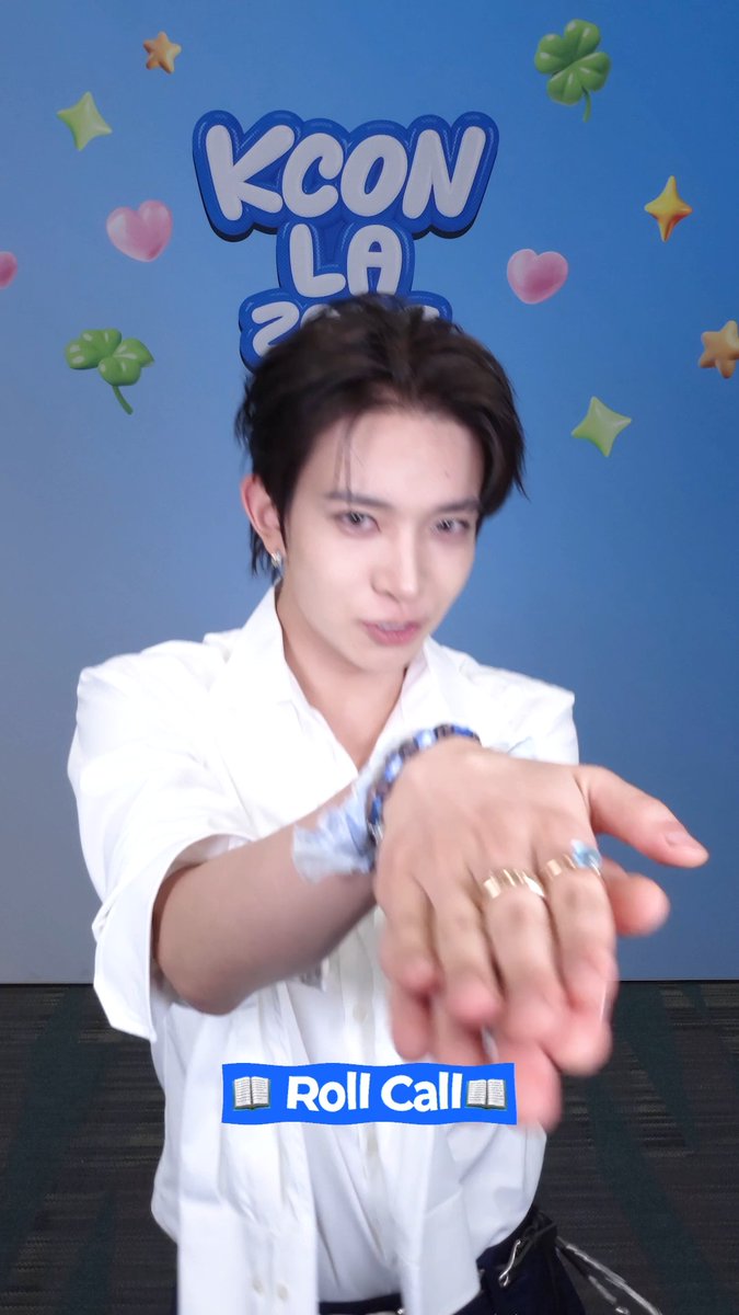 A young man with dark hair, wearing a white shirt and rings, reaches toward the camera in front of a blue "KCON LA" backdrop decorated with stars and hearts. A "Roll Call" label appears at the bottom, matching the post's invitation for attendees to check in for KCON DAY 3 at Crypto.com Arena.