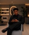 The image shows a young man sitting on a gray chair in a softly lit room with shelves and a circular mirror behind him. He appears thoughtful and composed, fitting the reflective nature of the post asking where one would invest $1,000 in Web3 today.