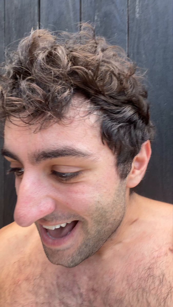 The image features a man with curly hair, who appears to be shirtless or at least not wearing a shirt. He has a big smile on his face as he looks towards the camera. The caption of the image reads "I accidentally fat fingered a $1.5m HYPE trade". This phrase is likely an inside joke or reference to a popular internet meme, and it adds a humorous element to the scene with the man's cheerful expression.