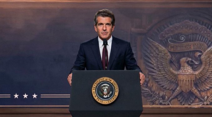 A scene featuring a man in a dark suit standing at a podium bearing the Seal of the President of the United States, with an eagle emblem visible on the wall behind him.