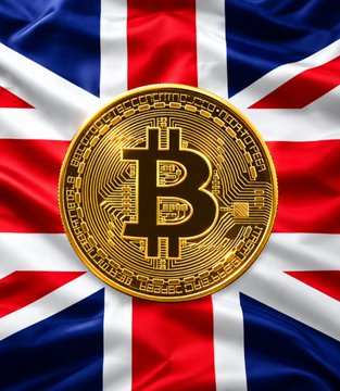 A golden Bitcoin coin is prominently displayed against a backdrop of the Union Jack flag. The image represents the UK's growing involvement in digital currencies, complementing news of Lloyds completing its first cross-border stablecoin settlement with Visa for 24/7 transactions.