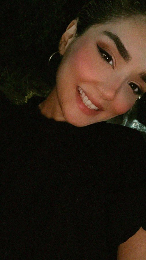 A nighttime selfie of a smiling young woman with dark hair, wearing a hoop earring and a dark top.
