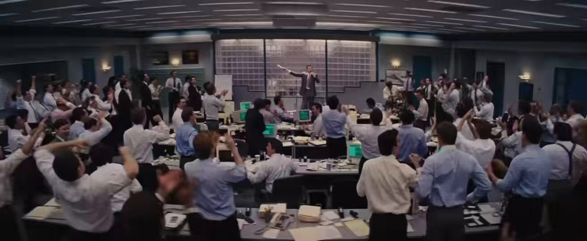 The image shows a group of people gathered around tables with computers and other equipment, suggesting that they are working together on a project or attending an event related to cryptocurrency or blockchain technology. The crowd appears engaged and focused on their tasks at hand.