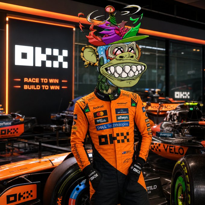 An F1 race team garage scene with the OKX logo prominently displayed alongside the tagline 'Race to Win, Build to Win,' showing a driver in an orange McLaren racing suit with a stylized cartoon mascot head.